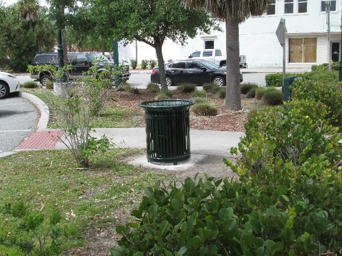 Photo of a trash can in a parking lot green space.