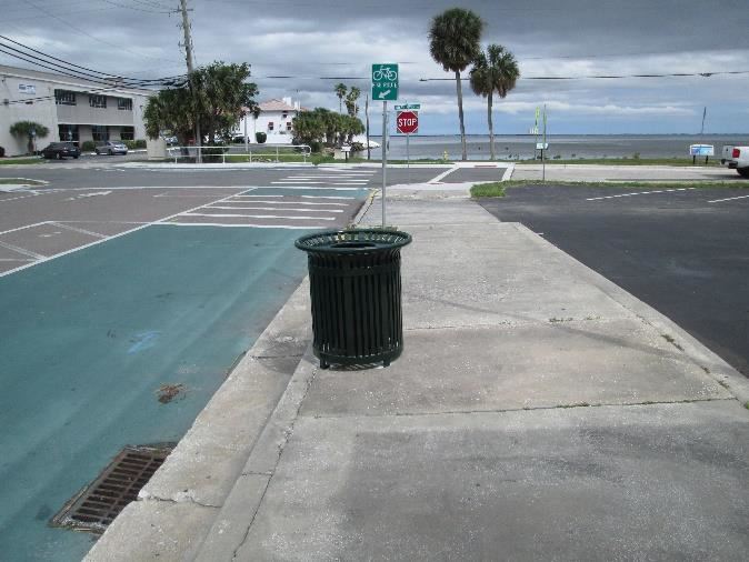 Photo of a trashcan on a sidewalk along a street.
