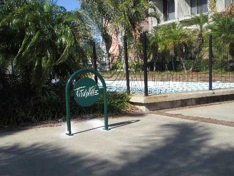 Photo of a green rounded bike rack in front of palm trees and a building.
