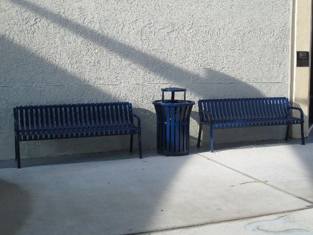 Photo showing dark blue metal benches and a trashcan in a courtyard.